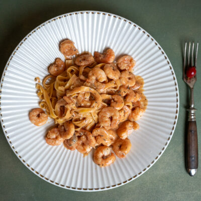 ein Teller mit Tagliatelle und Garnelen, daneben eine rustikale Gabel mit darauf liegender Hagebutte
