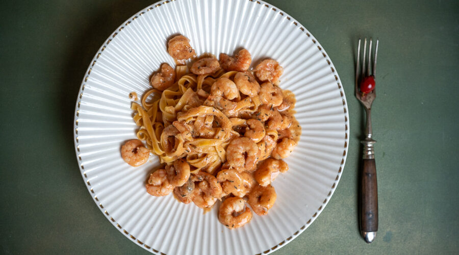 Tagliatelle mit Garnelen in Hagebutten-Thymian-Sud ein Teller mit Tagliatelle und Garnelen, daneben eine rustikale Gabel mit darauf liegender Hagebutte