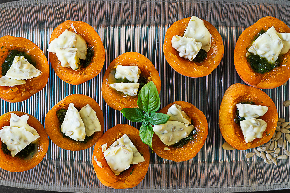 mit Basilikum-Pesto gefüllte Aprikosenhälften, auf denen stückige weiße Schokolade mit Sonnenblumenkernen und Pinienkernen drapiert ist