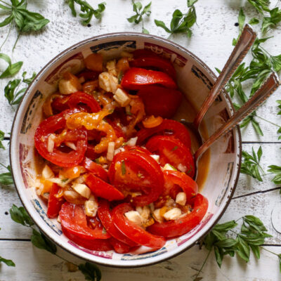 eine Schüssel Tomaten-Aprikosensalat mit Waldmeister auf einem weißen Holzbrett umgeben von getrocknetem Waldmeister
