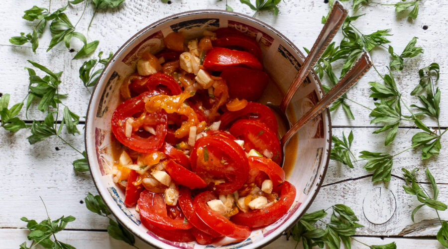 eine Schüssel Tomaten-Aprikosensalat mit Waldmeister auf einem weißen Holzbrett umgeben von getrocknetem Waldmeister